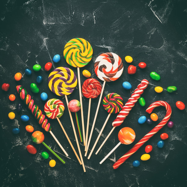 彩色的棒棒糖和彩色的圆糖果在黑色的石头背景，色调。节日的甜蜜的背景。俯视图，平放，复制空间。广场的照片。图片下载