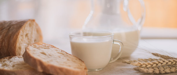 清淡的乡村早餐——在窗边的桌子上有切好的乡村面包，一个罐子和一杯牛奶，亚麻餐巾，晨光，全景图片下载