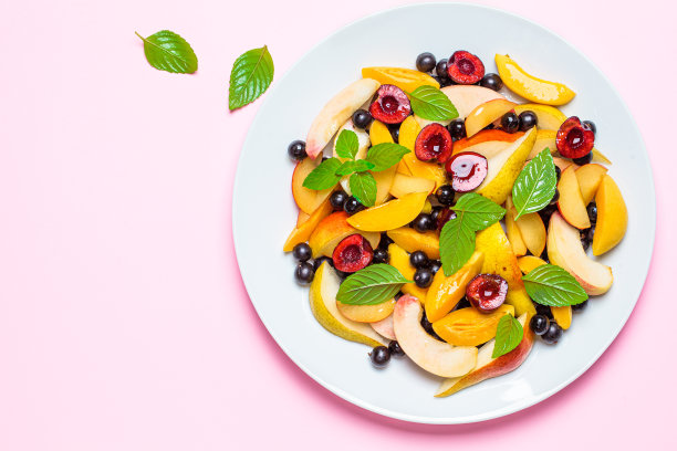 水果沙拉与浆果在白色的盘子，粉红色的背景，俯视图。健康素食的概念。素材图片