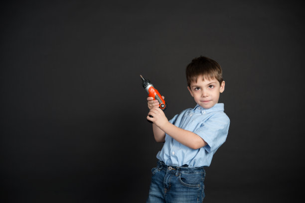 一个穿着蓝色衬衫的小男孩透过放大镜看着画室里那台在黑暗背景下被拆解的电脑。电脑组装。图片下载