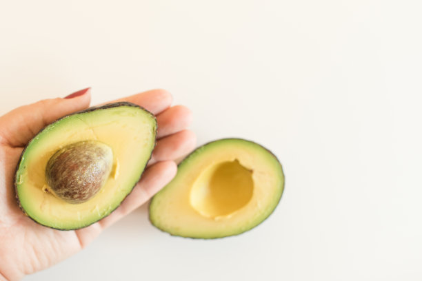 女人的手拿着一个白色背景的一半哈斯鳄梨图片下载
