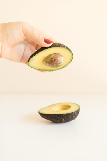 女人的手拿着一个白色背景的一半哈斯鳄梨图片下载