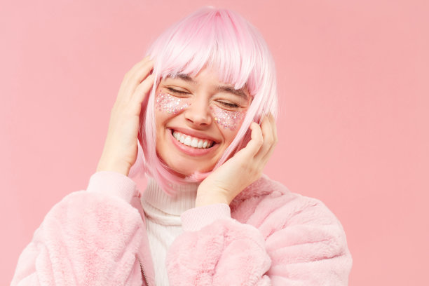 年轻快乐的女孩穿着毛皮大衣，粉红色的头发，触摸着她的头，闭着眼睛随着音乐跳舞，在工作室背景孤立图片下载