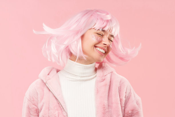 年轻快乐的女孩闭着眼睛，穿着裘皮大衣，跳舞和移动的头，所以她的头发是飞舞的，孤立在粉红色的背景图片下载