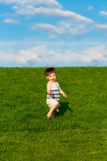 快乐的蹒跚学步的孩子在草坪上奔跑，明亮的绿色草地和蓝色的天空图片下载