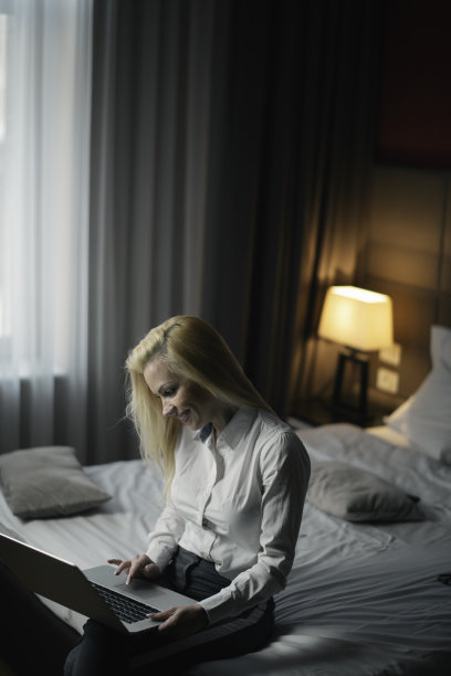 美丽的年轻女子在酒店房间的笔记本电脑上工作图片下载