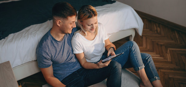 顶视图照片的白人妇女和她的情人坐在地板上，微笑着使用平板电脑图片下载