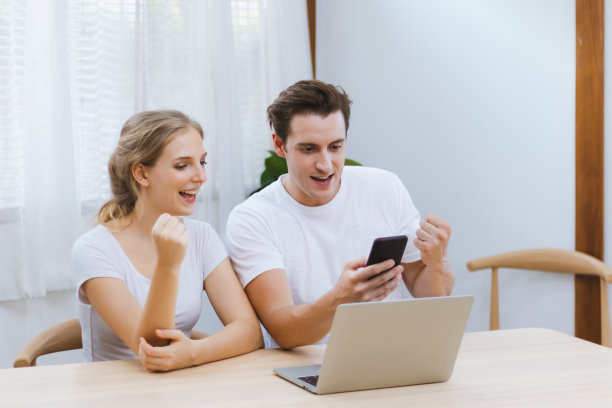 微笑的白人夫妇一起庆祝成功的企业家在线业务或工作成就或教育考试成绩在家里通过智能手机。互联网和技术照片的概念图片下载