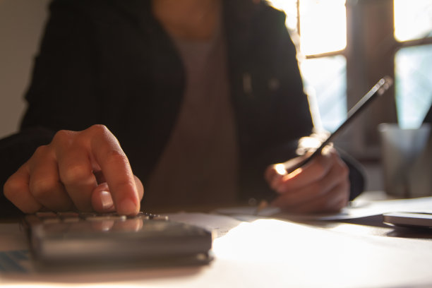 商人手用计算器计算奖金(或其他补偿)给员工以提高生产力。选择焦点在日落的书桌上写论文图片下载