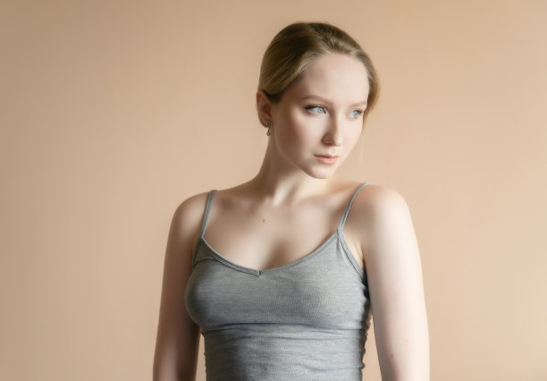 一个女人靠着米色的墙摆姿势。图片下载