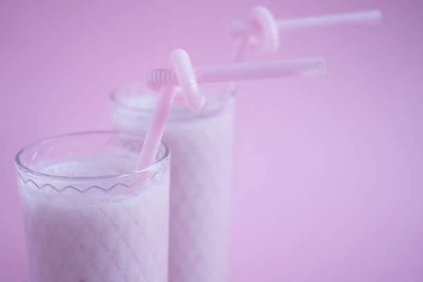 特写的单色照片与粉红色的冷水果冰沙和饮用吸管在粉红色的背景。夏天喝奶昔。图片下载