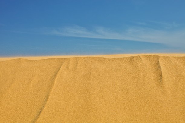明亮的蓝色天空和海洋背景上的沙丘。图片下载