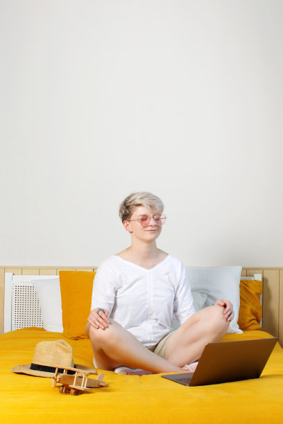 金发漂亮的年轻时髦的女人坐在床上的笔记本电脑在网上冥想拂晓图片下载