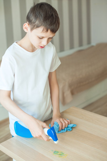 一个少年把清洁剂放在桌子上。他手里拿着一块蓝色的布来擦去污垢。清洁、秩序、纪律的观念。垂直图图片下载