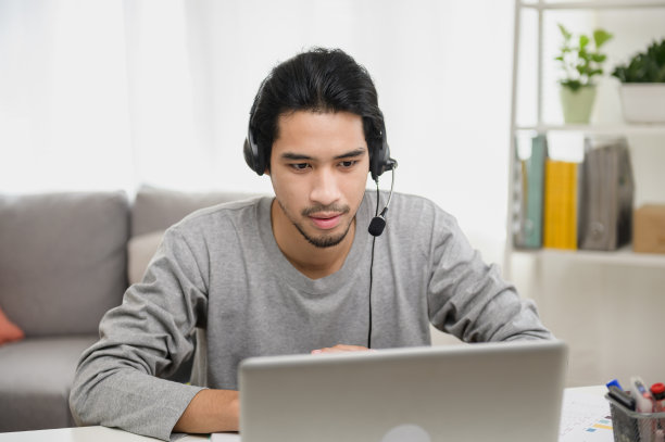 聪明的亚洲人在自我隔离期间与业务同事朋友进行视频通话的肖像照片。一个男人戴着耳机看着摄像机。图片下载