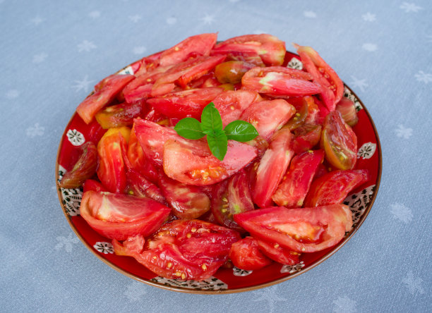 灰色桌布上的红色盘子里放着几片新鲜多汁的牛心番茄和罗勒图片下载