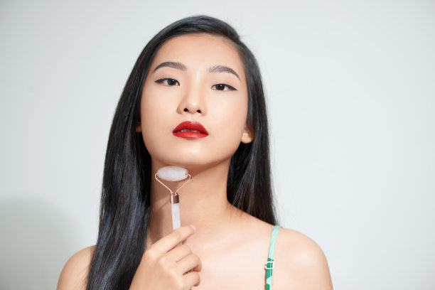 一个年轻女子的近距离照片看起来轻松和微笑，而使用天然玫瑰石英脸部滚轮图片下载