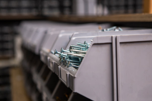 在工具和配件商店的架子上，集中在塑料盒子里的白色银色螺丝。图片下载