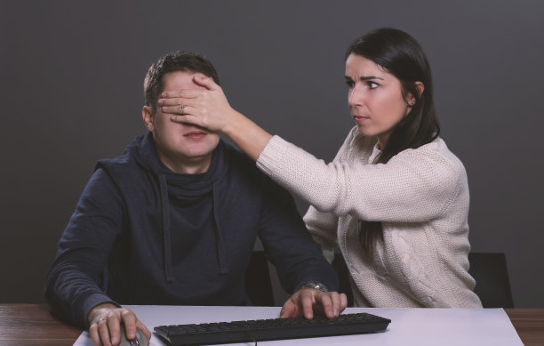 女朋友妨碍她的男友，而他正试图看成人内容的网上，她的手捂住他的眼睛。生气的女朋友图片下载