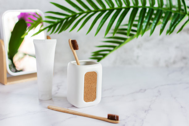 茶杯里装着竹子牙刷，浴室里白色大理石桌上放着牙膏和镜子。图片下载