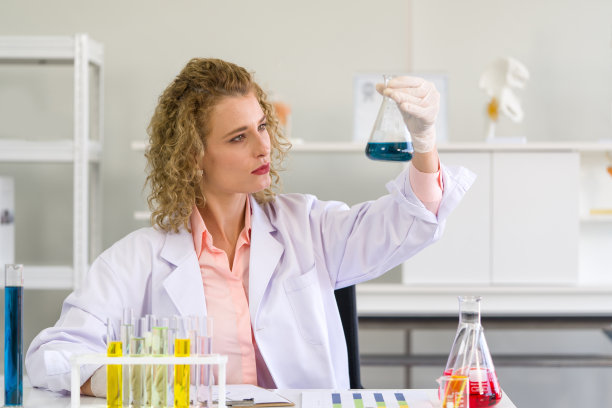 这位年轻的金发科学家正在考虑化学物质的颜色，以观察酸性和碱性。化学实验室的工作气氛。素材图片