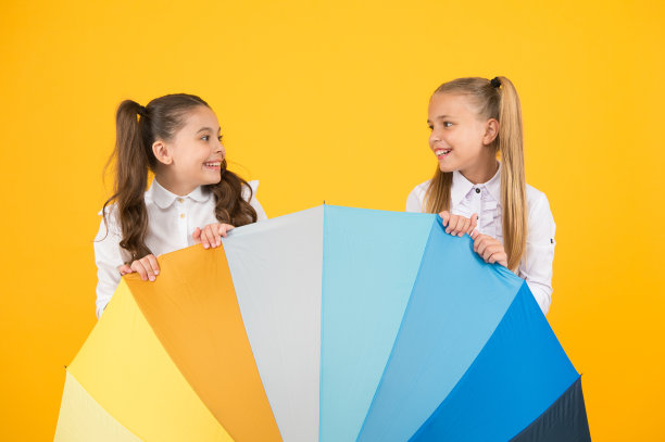 雨消失。小女生们在鲜艳的雨伞后面微笑。黄色的背景下，快乐的孩子们在雨中步行上学。阳光和雨水才能形成彩虹图片下载