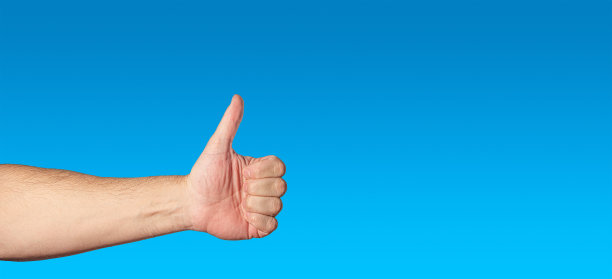 男子赤裸的手显示一个手势拇指向上，作为一个类似或协议孤立在蓝色梯度背景蓝色天空与文本复制空间。图片下载