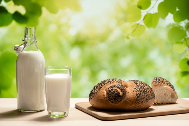 切菜板上放着一瓶牛奶、一只玻璃杯和一条面包图片下载
