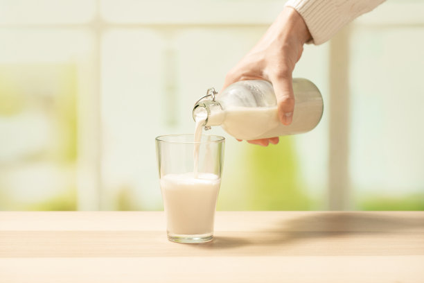 一位穿着白色毛衣的妇女将牛奶从瓶子里倒进空杯子里图片下载