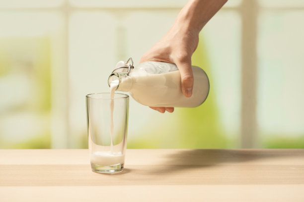 一个女人的手把牛奶从瓶子里倒进空杯子里图片下载
