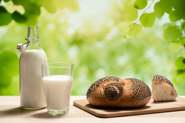 切菜板上放着一瓶牛奶、一只玻璃杯和一条面包图片下载