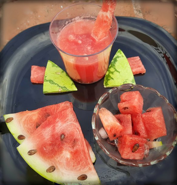 将西瓜汁切片冷藏，将冰块放在玻璃碗中，将西瓜片放在黑色的盘子中，适合夏季食用，也是健康水果和保持身体水分的饮料图片下载