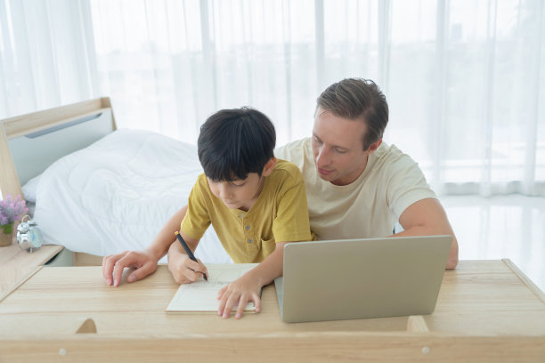 快乐微笑的金发商人，伙计。自由职业者在家工作和他的儿子，学生在网上教作业用笔记本电脑笔记本隔离。家庭爸爸、孩子和教育理念。图片下载