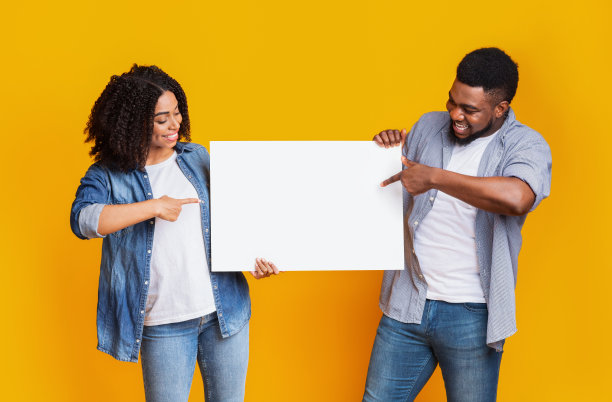 一对兴高采烈的黑人夫妇手持黄色背景的空白广告牌并指着图片下载