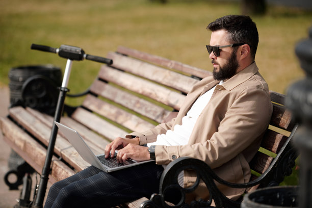 年轻的商人带着移动设备坐在公园里上网图片下载