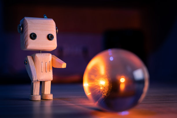 一个小的木制玩具机器人在黑暗中看着一个神奇的玻璃球。墙纸,长途跋涉的背景。低光图片下载