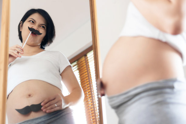 有趣的亚洲年轻孕妇看着镜子，留着小胡子图片下载