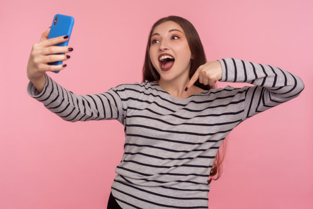 在视频通话中，迷人的快乐的女人在条纹运动衫指着手指向下的肖像图片下载