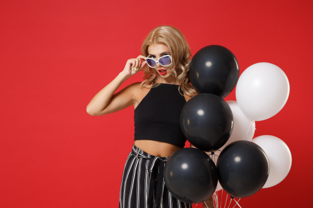 漂亮的年轻女子女孩在黑色的衣服，眼镜摆出孤立的红色背景。2020年新年快乐，生日节日派对概念。模拟拷贝空间。庆祝，举着气球。图片下载