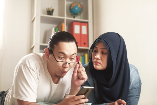 亚洲穆斯林妇女看起来嫉妒她的丈夫做男人与其他女孩在电话聊天，糟糕的夫妇关系图片下载