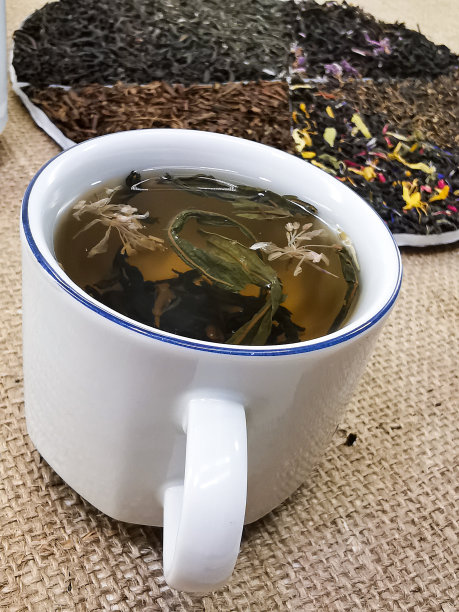 健康的生活方式的概念。将绿茶和红茶混合加入花的混合物。茶是在杯子里泡的。照片背景是粗麻布。图片下载