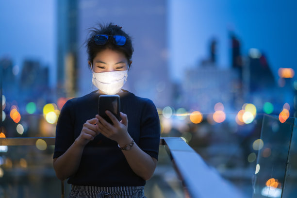 迷人的亚洲女性女性戴着护手面罩，用智能手机技术与背景光谷城市建筑背景的商业理念理念沟通图片下载