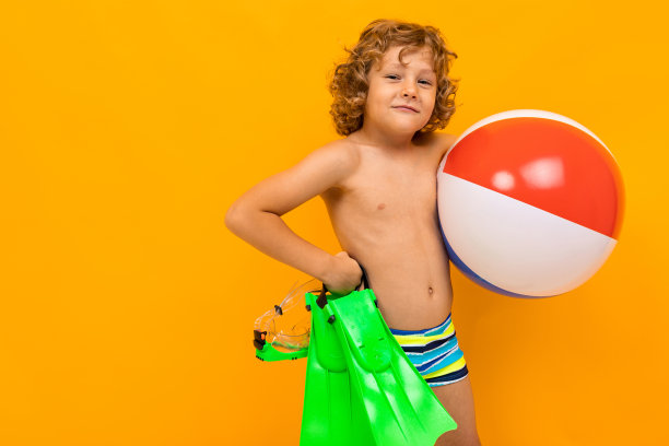 在画室里，一个欧洲红发卷毛男孩拿着脚蹼在黄色背景下游泳和游泳图片下载