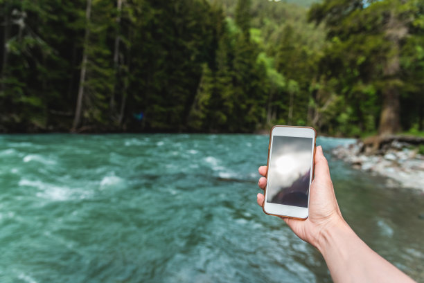 第一人称视角的女性手与手机在一个美丽的河流和森林的背景在山里在夏天。度假旅游传播理念图片下载