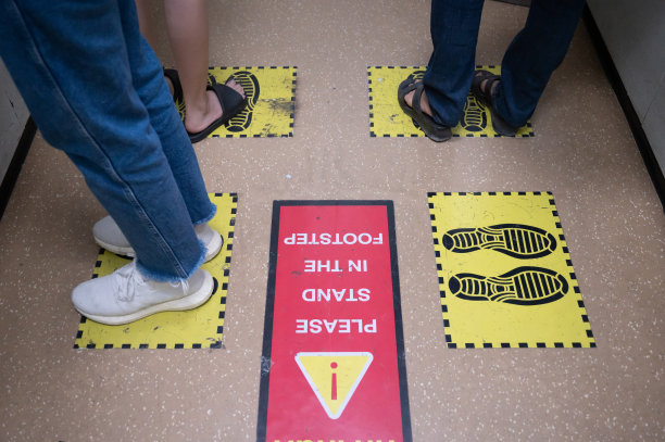 在新冠肺炎大流行期间，电梯或电梯内站在黄色脚印标志上的人的脚，为防止病毒传播预留空间。图片下载