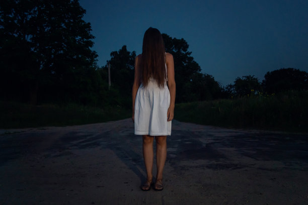 黑暗中，一个成年女孩站在十字路口，穿着白色的裙子，把长发翻过来。恐怖，神秘主义的概念图片下载