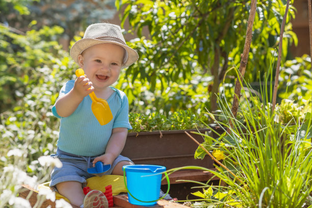 微笑的小男孩拿着塑料耙坐在户外。图片下载