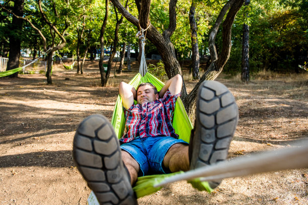 一个男人正在吊床上休息。休息日和休息。在一个阳光明媚的日子里，一个年轻英俊的小伙子带着一本书躺在一个吊床上图片下载