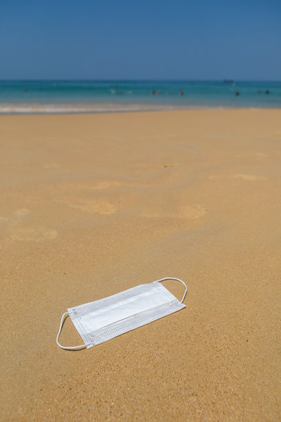 海滩上的沙滩上躺着一个医用防护口罩。COVID-19很危险图片下载