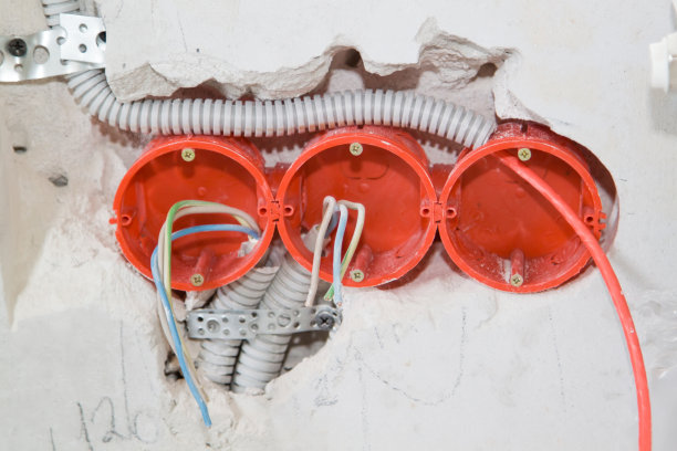 在灰色水泥墙内的洞中伸出电线和电缆，为正在施工的房屋供电做准备。电缆敷设在墙槽的保护波纹中图片下载